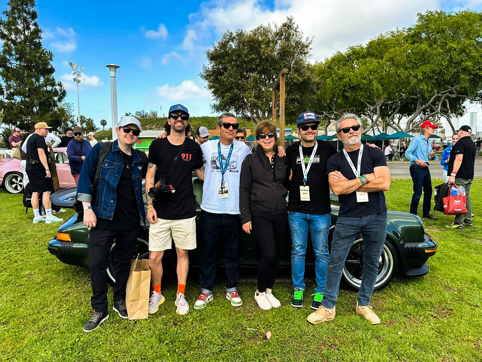 Grupo de personas posando junto a un coche clásico verde en un evento al aire libre de cultura del automóvil.
