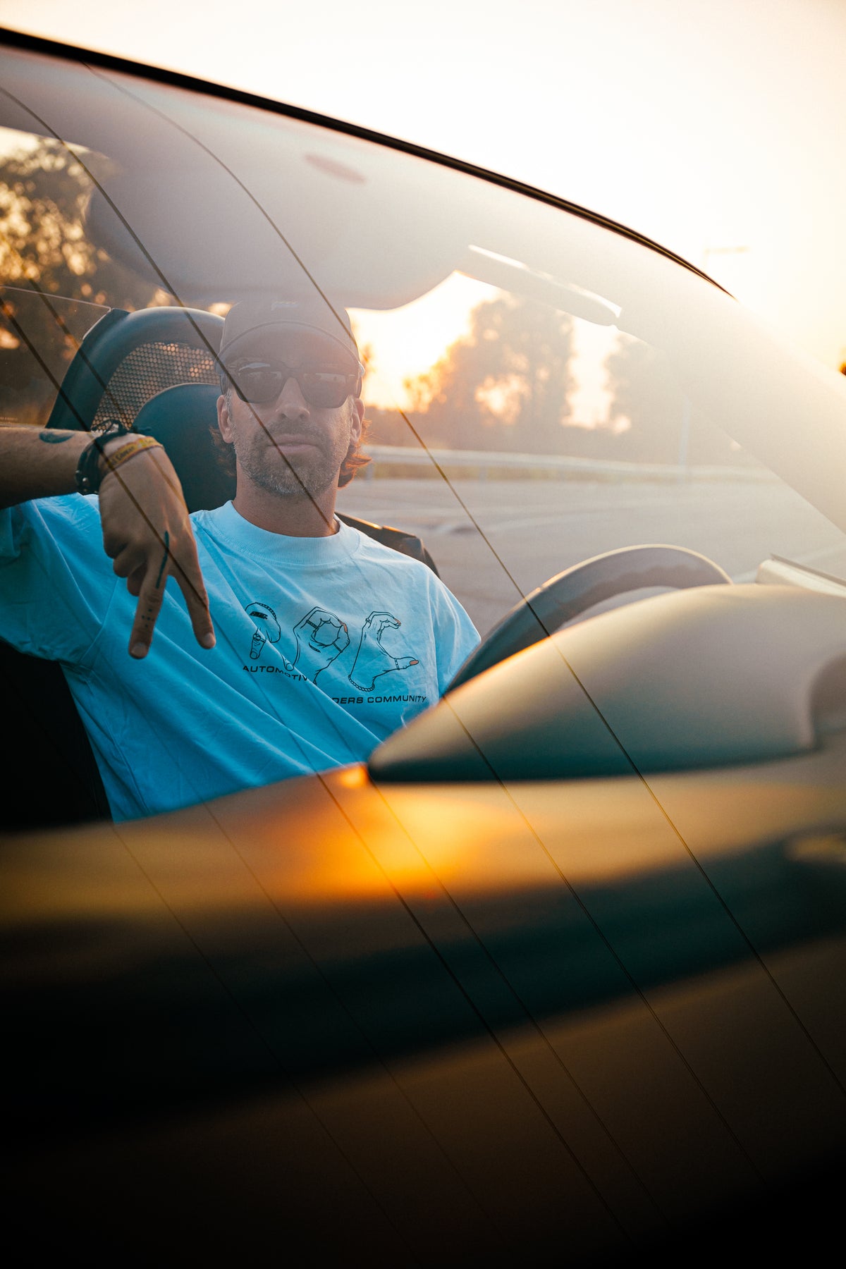 Camiseta AOC Hands White con gráfico frontal de manos, usada por modelo en coche descapotable al atardecer