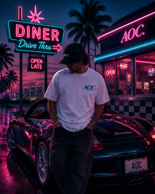 Camiseta Porsche Boxster 986 DriveThru blanca con logo AOC en el pecho, usada por modelo junto a coche negro en diner con neones