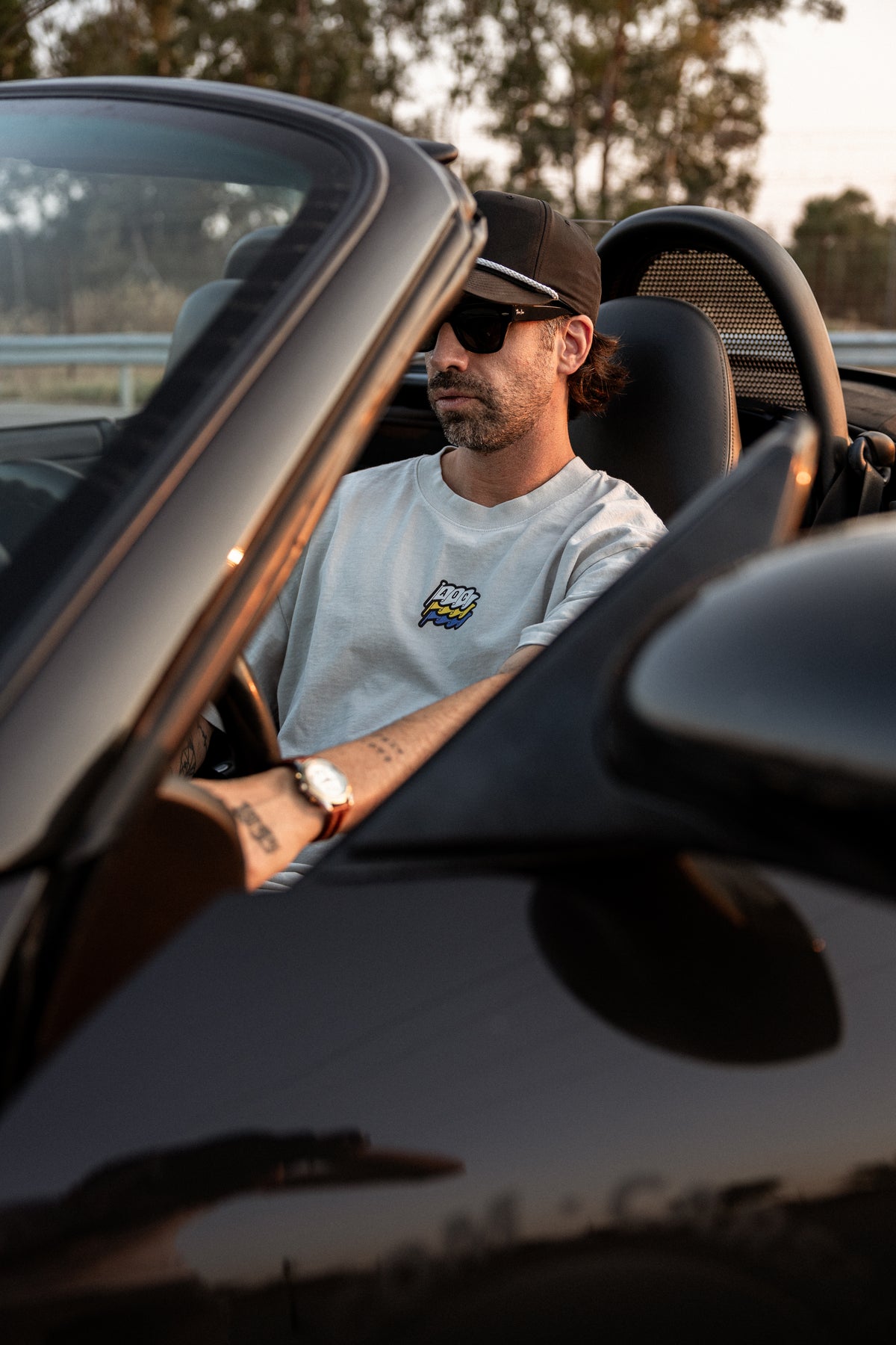 Camiseta Racers Club Midnight Series con logo en el pecho, usada por modelo dentro de coche descapotable negro