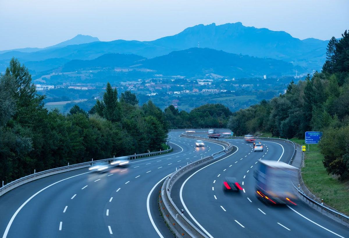 Carretera entre árboles y montañas con coches en movimiento