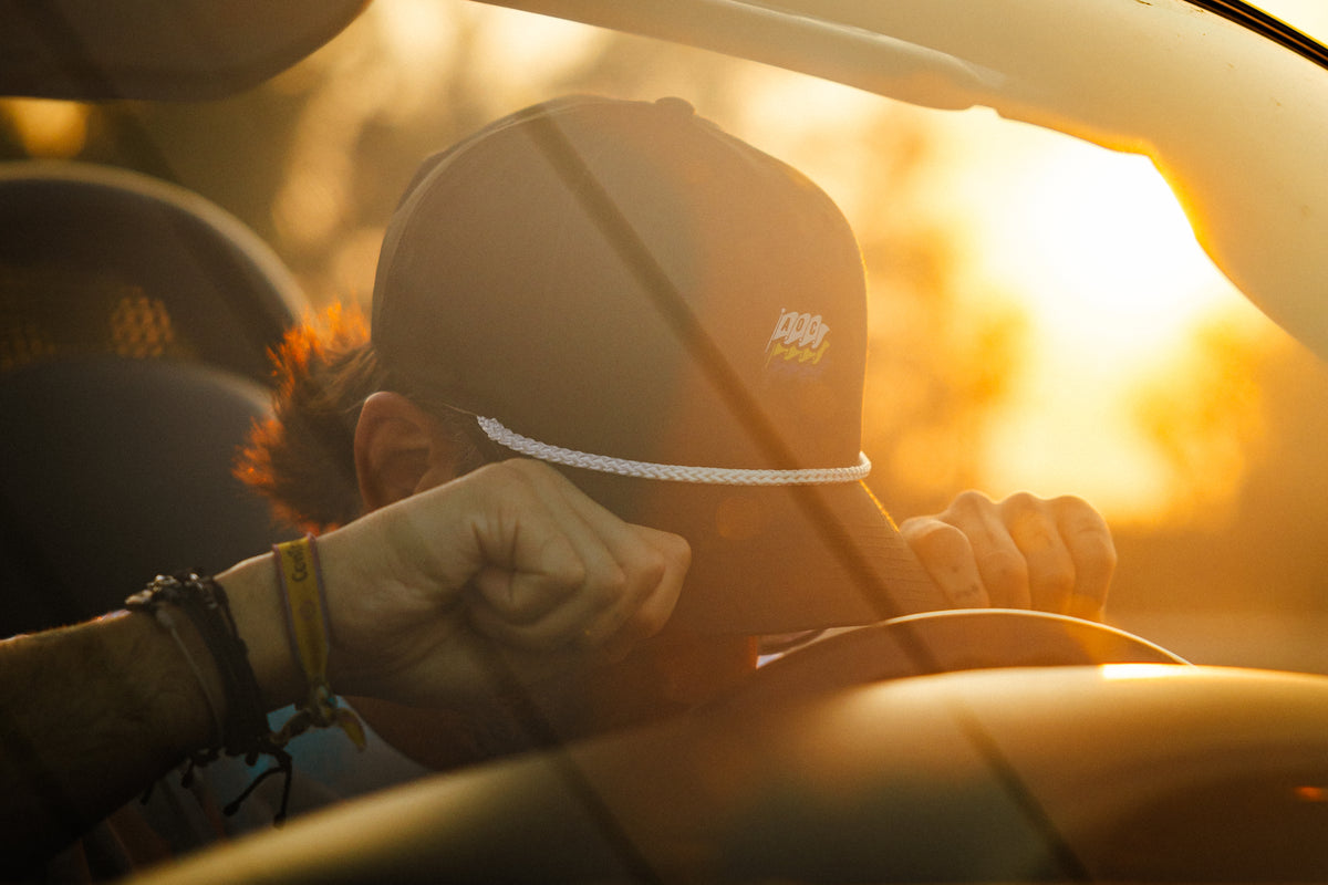 Koke Muñoz ajustándose una gorra AOC dentro de un Porsche Boxster al atardecer