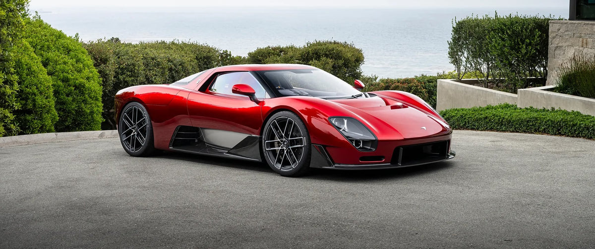 McLaren McL 6GT rojo en exterior junto a una casa moderna con vistas al mar